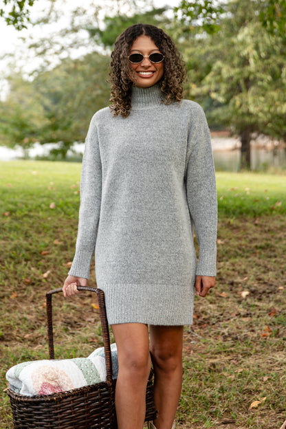 Woman wearing a gray sweater dress standing outdoors with a basket.