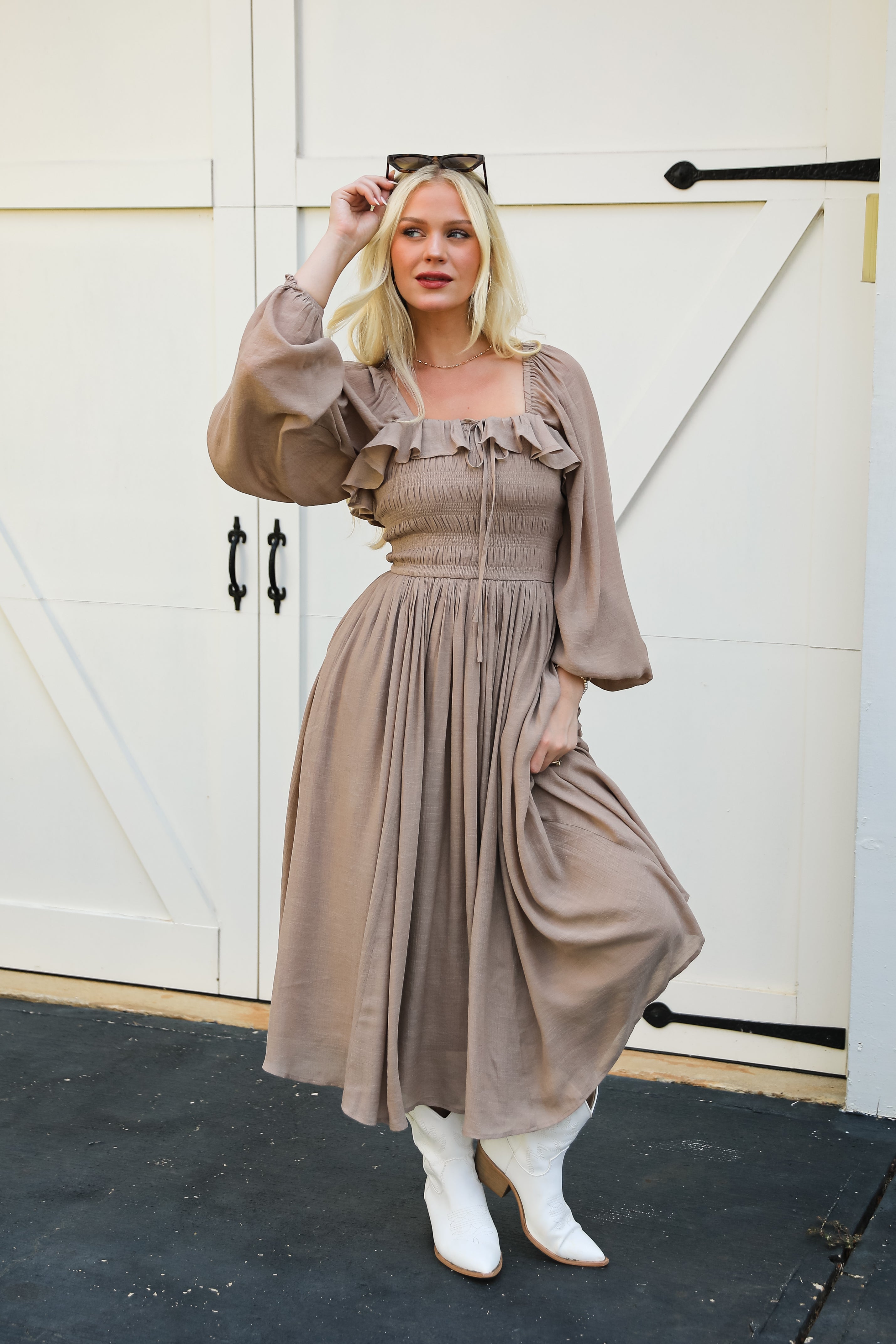 Woman wearing a brown dress with ruffled sleeves in front of a white door.