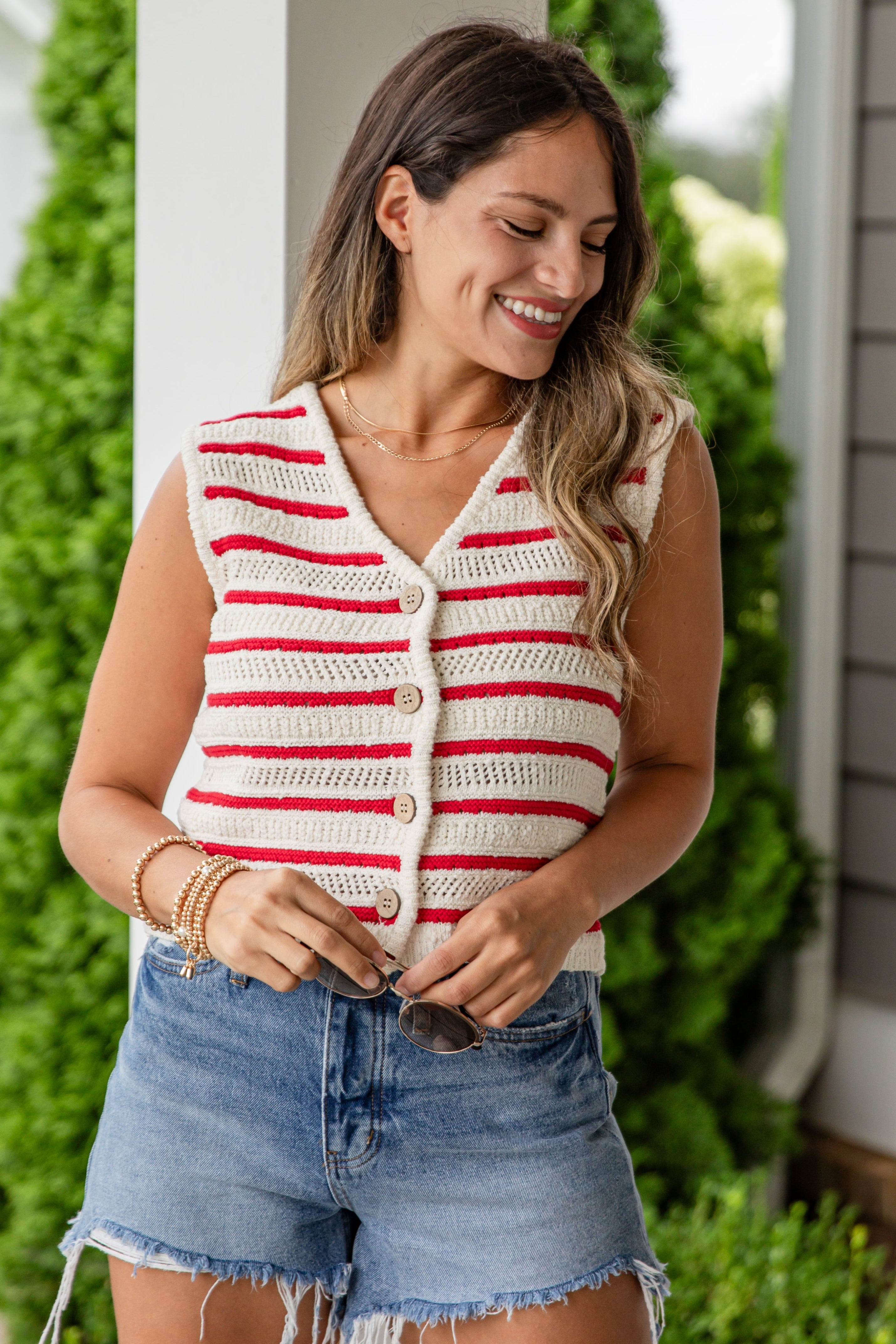 Woman wearing a red and white striped vest and denim shorts standing outdoors.