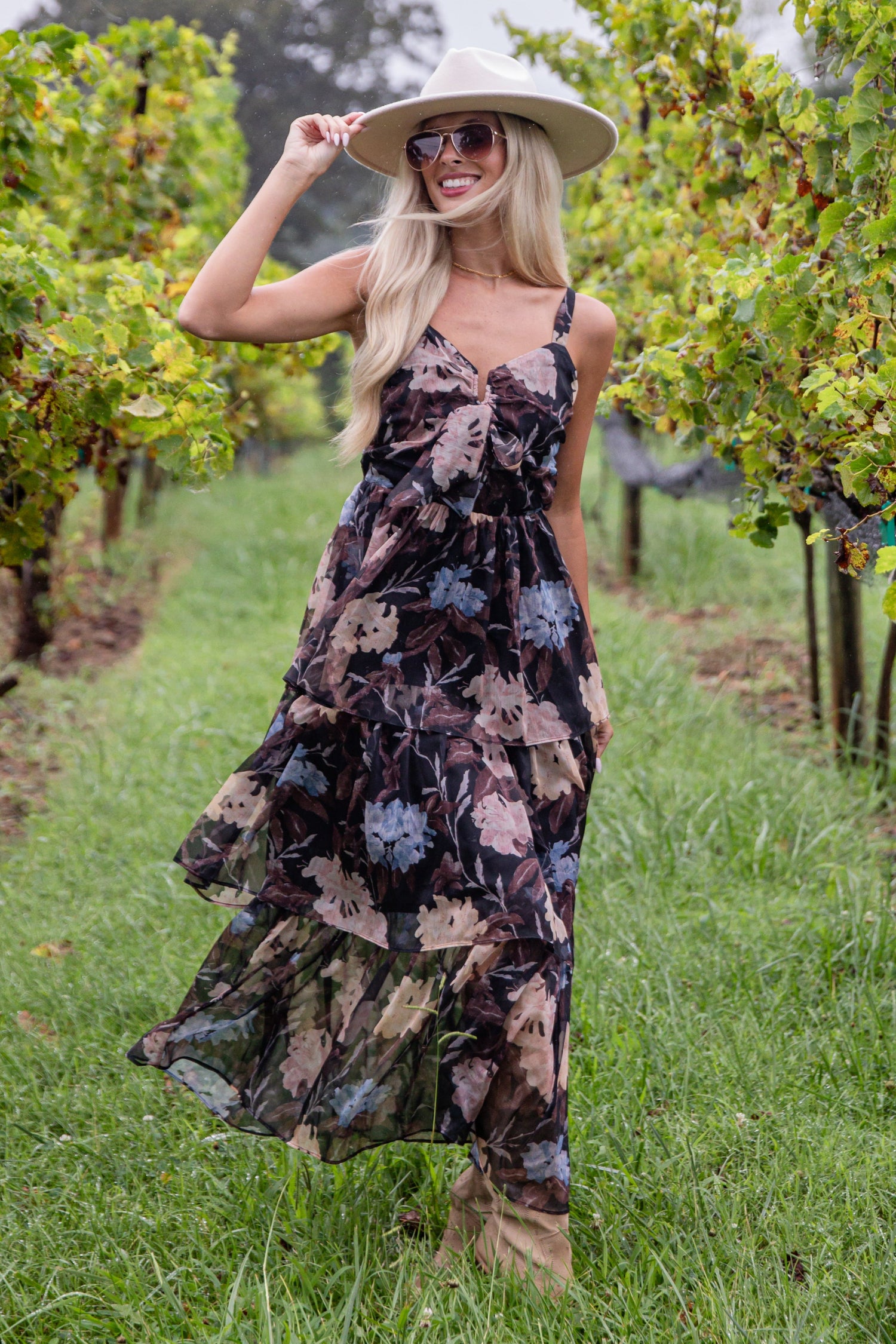 Woman in a floral dress and hat standing in a vineyard