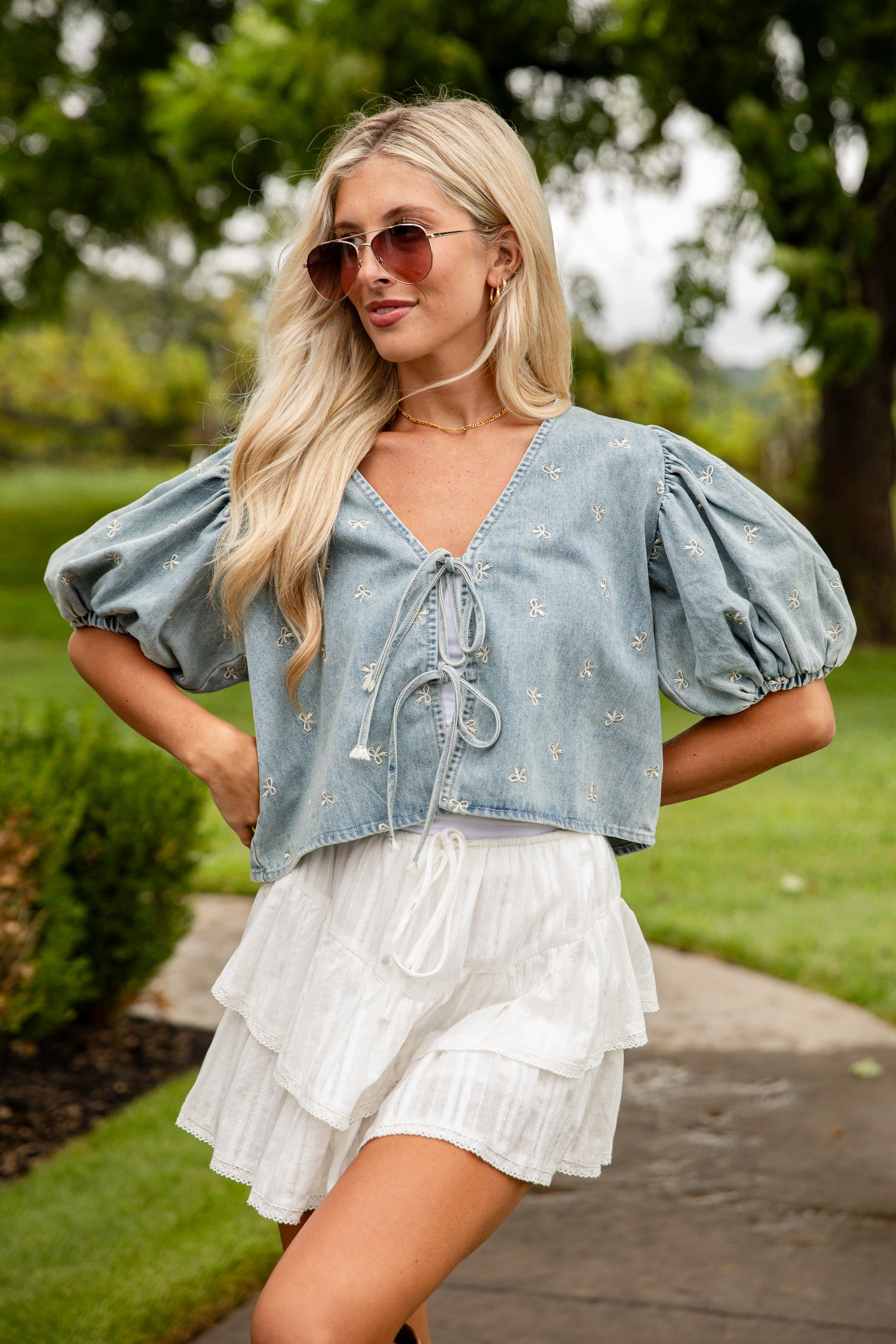 Woman wearing a denim top with puff sleeves and a white skirt outdoors.