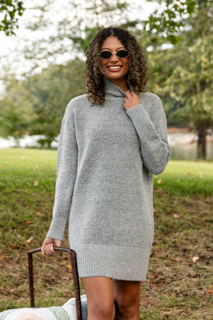 Woman wearing a gray sweater dress outdoors with trees in the background