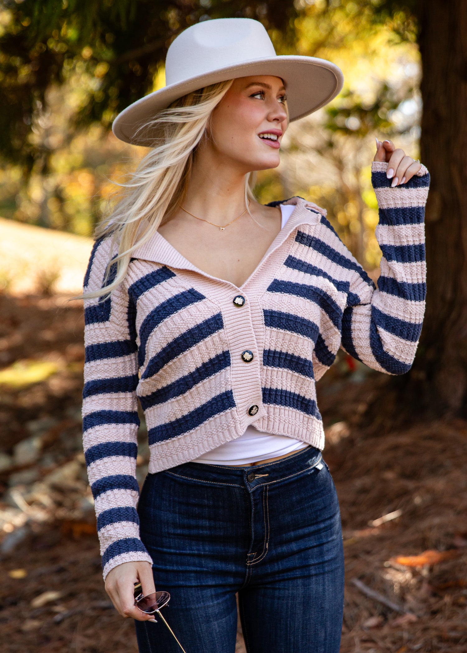 Woman wearing a striped cardigan, white hat, and sunglasses outdoors.
