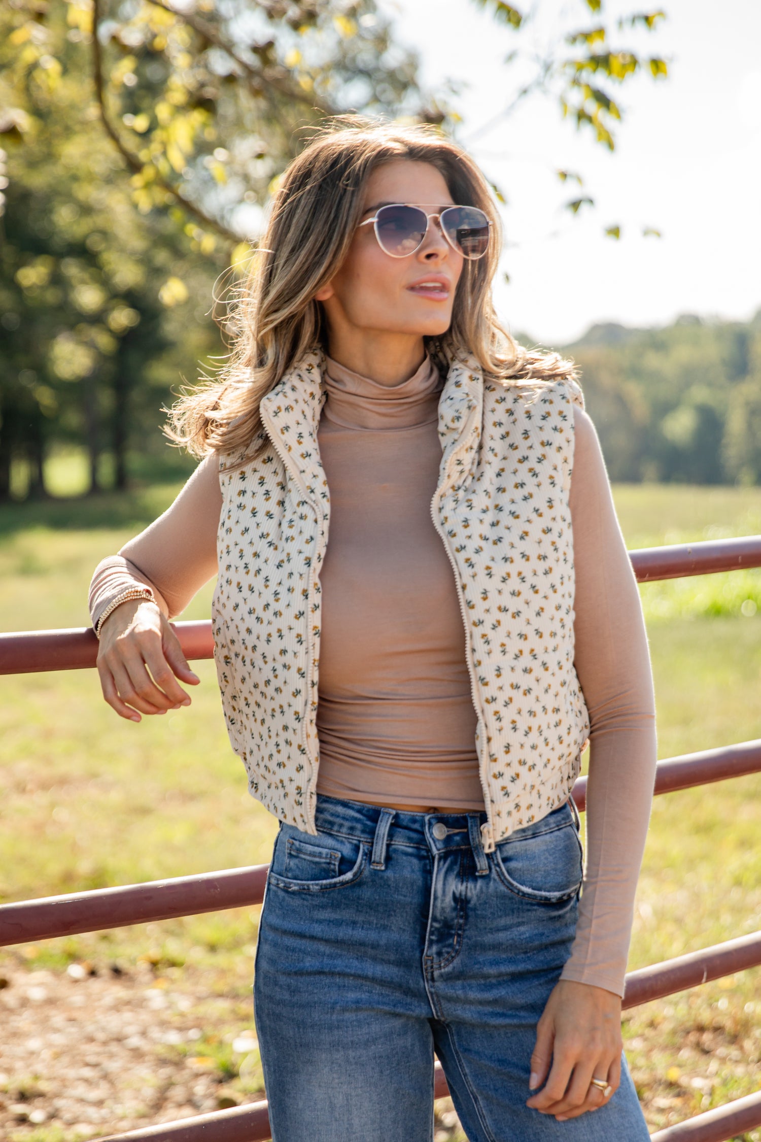 Woman wearing a leopard print vest, beige turtleneck, and blue jeans outdoors.