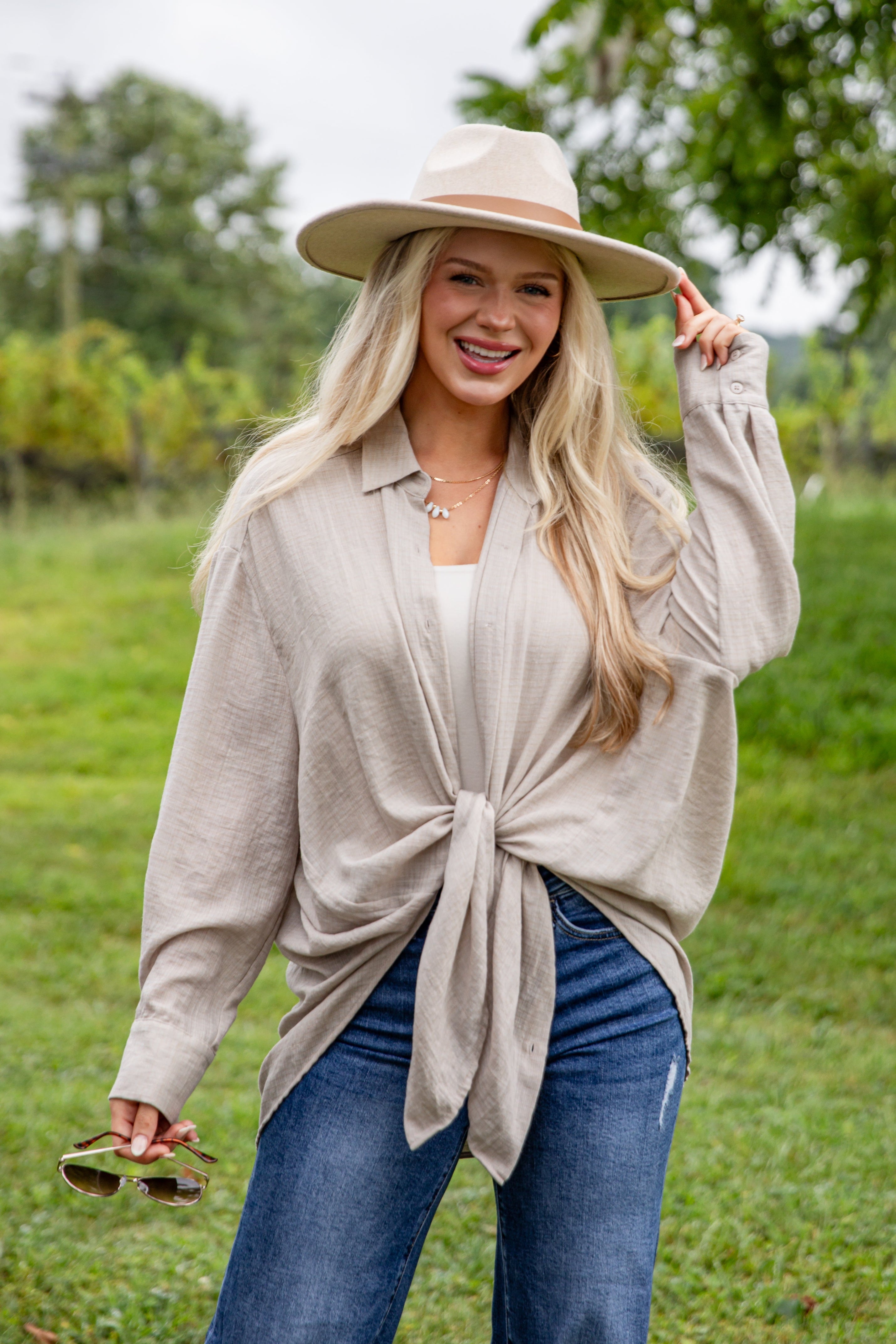 Woman wearing a beige cardigan, blue jeans, and a beige hat outdoors.