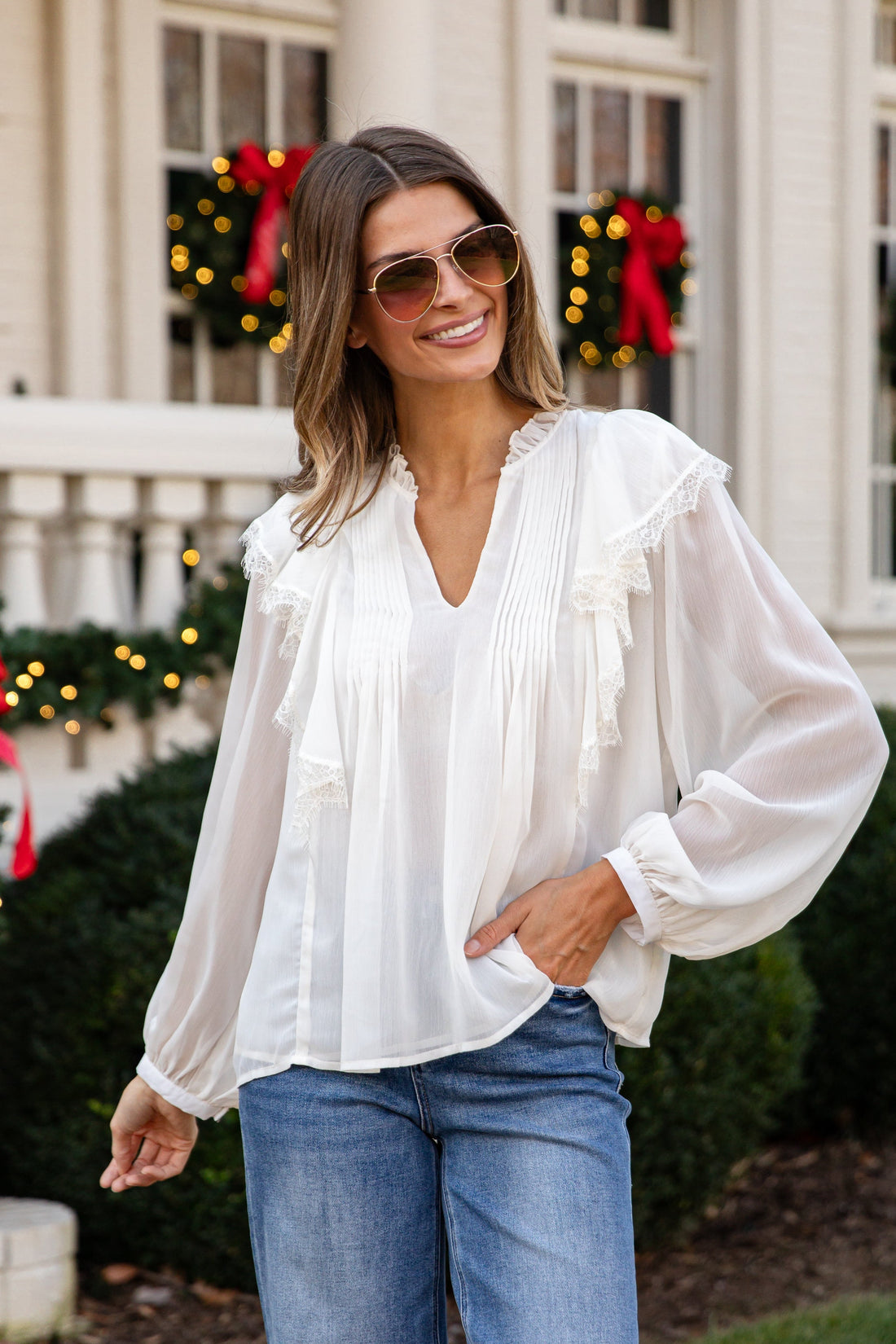 Woman wearing a white blouse and blue jeans standing in front of a decorated house.