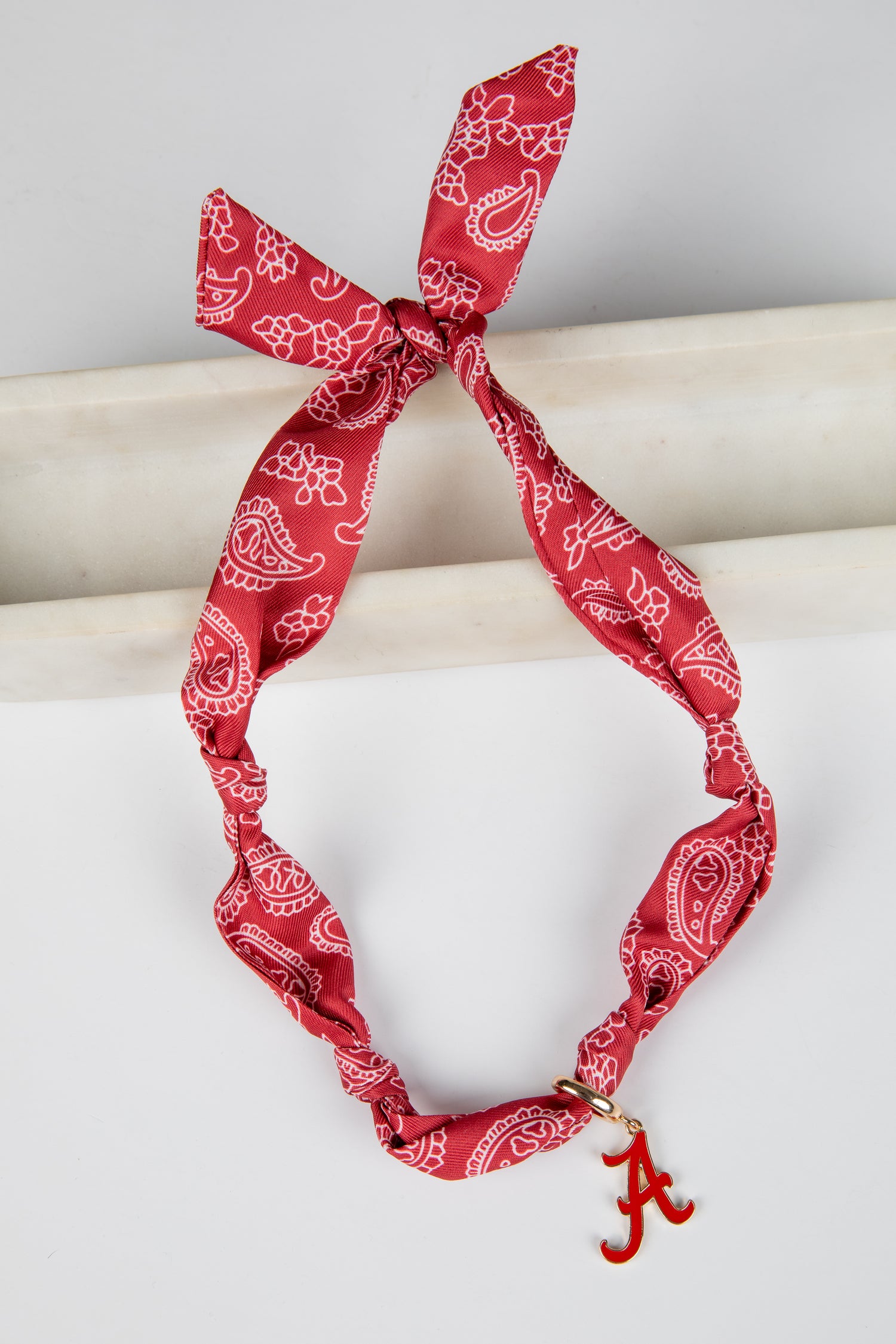 Red bandana with white patterns tied around a cylindrical object on a light gray background