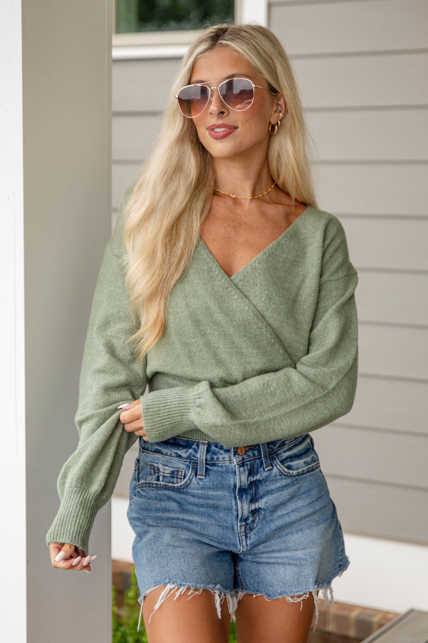 Woman wearing a green sweater and denim shorts outdoors
