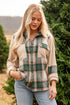 Woman wearing a plaid shirt and beige jacket in a Christmas tree farm setting