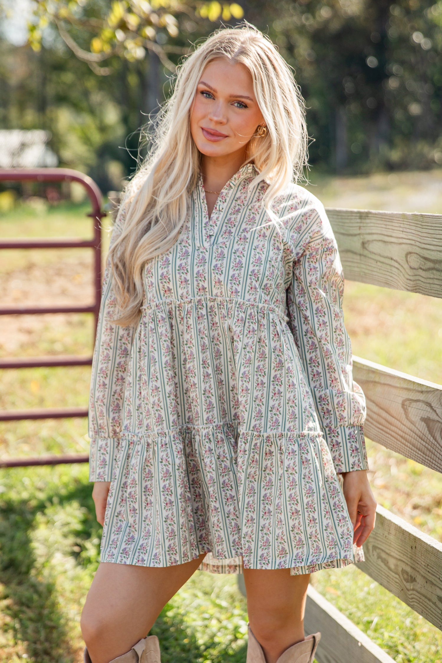 Woman in a patterned dress standing in a field with a wooden fence.