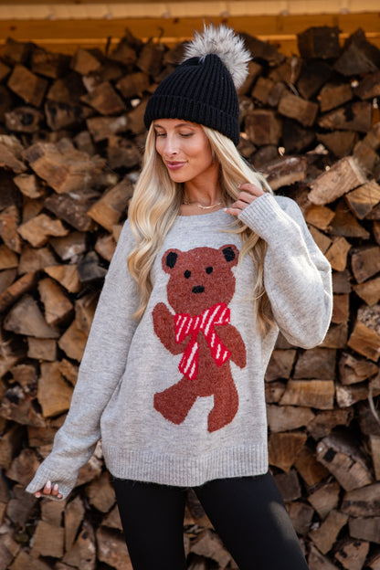 Woman wearing a sweater with a bear design in front of stacked firewood.