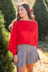 Woman wearing a red sweater and gray skirt standing in a Christmas tree lot.