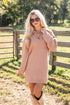 Woman wearing a pink sweater dress and sunglasses in a rural setting