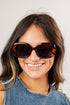 Woman wearing tortoiseshell sunglasses with a plain background