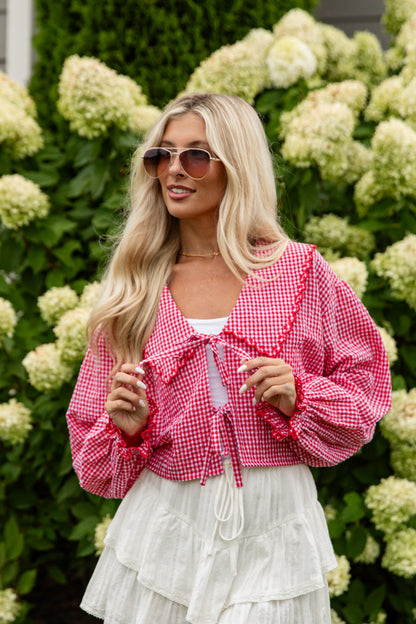 Woman wearing a pink checkered blouse and white skirt standing in front of green hydrangeas.