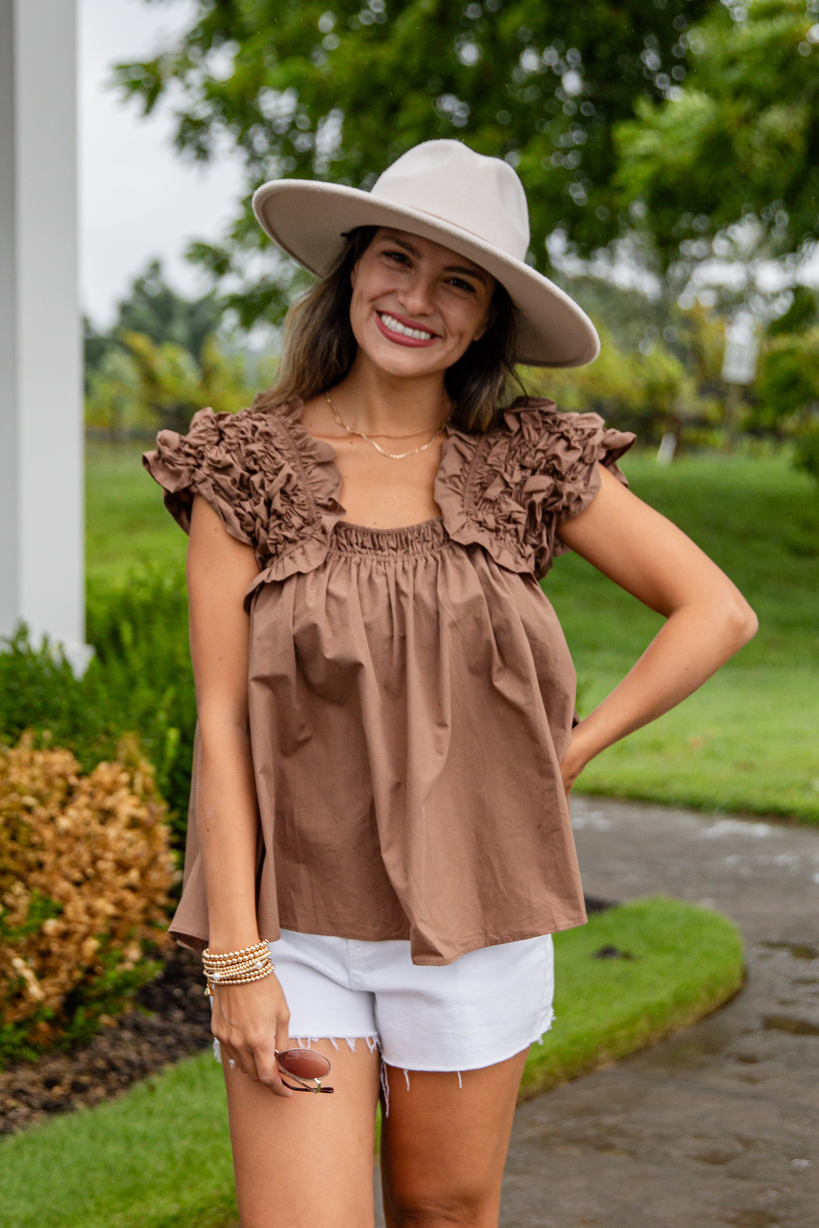 Woman wearing a brown ruffled top and white shorts outdoors.