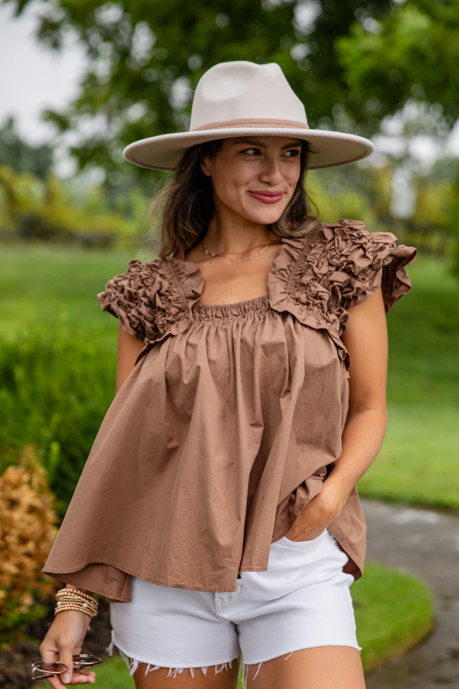 Woman wearing a brown ruffled top and white shorts outdoors.