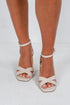 Beige high-heeled sandals worn by a person on a white background