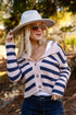 Woman wearing a striped cardigan, sunglasses, and a wide-brimmed hat outdoors.