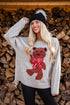 Person wearing a sweater with a teddy bear design in front of stacked wood.