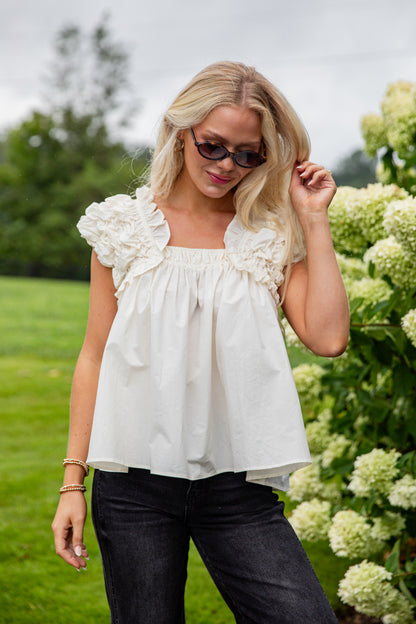 Woman wearing a white blouse with ruffled shoulders in a garden setting