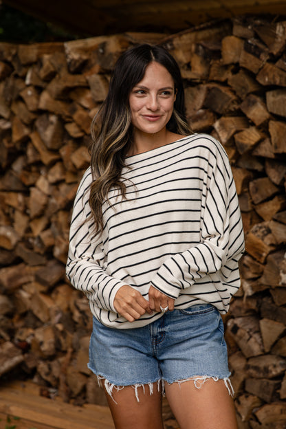 Woman wearing a striped sweater and denim shorts standing in front of stacked firewood.