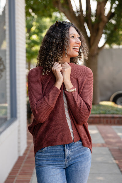 Woman wearing a brown sweater and blue jeans standing outdoors.