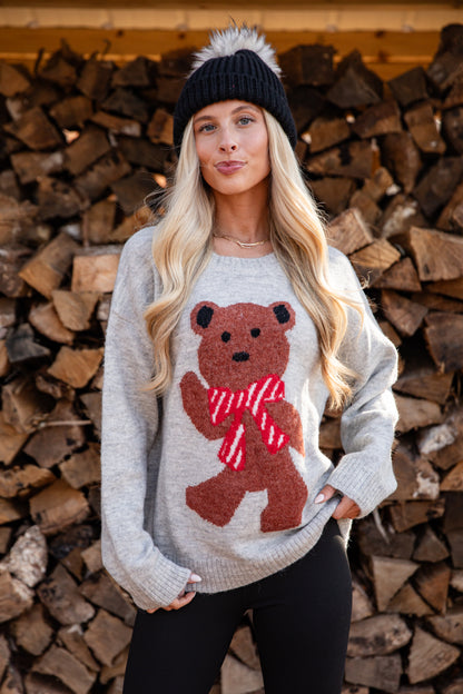 Woman wearing a sweater with a bear design in front of stacked firewood.