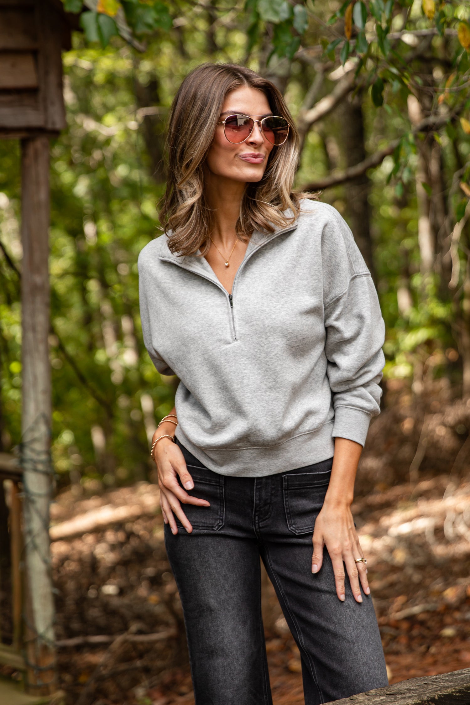Woman wearing a gray sweater and sunglasses in a forest setting