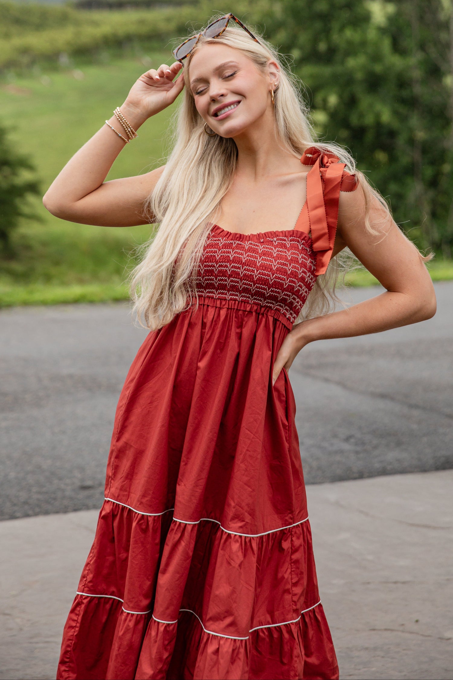 Woman in a red dress standing outdoors with greenery in the background