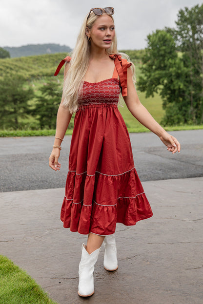 Woman in a red dress and white boots standing outdoors with greenery in the background