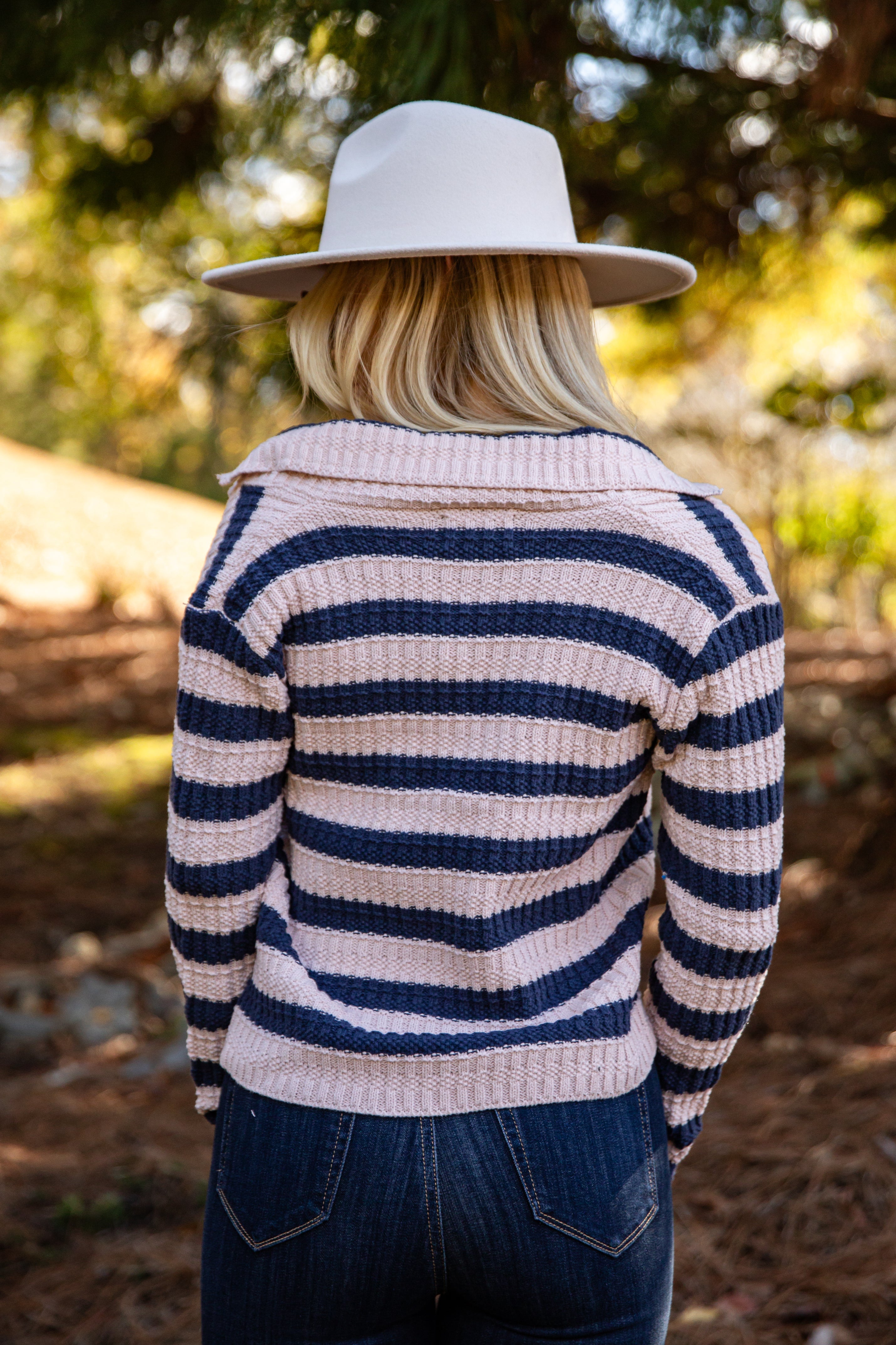 Person wearing a striped sweater and white hat in a forest setting
