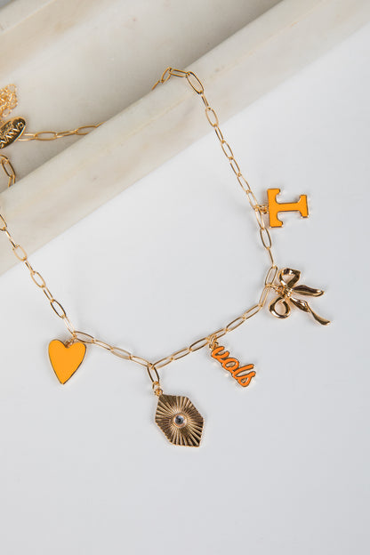Gold bracelet with various charms including a heart, bow, and initials on a white background
