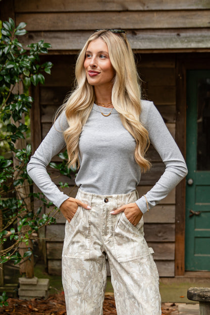 Woman wearing a gray long-sleeve top and light-colored pants standing outdoors.