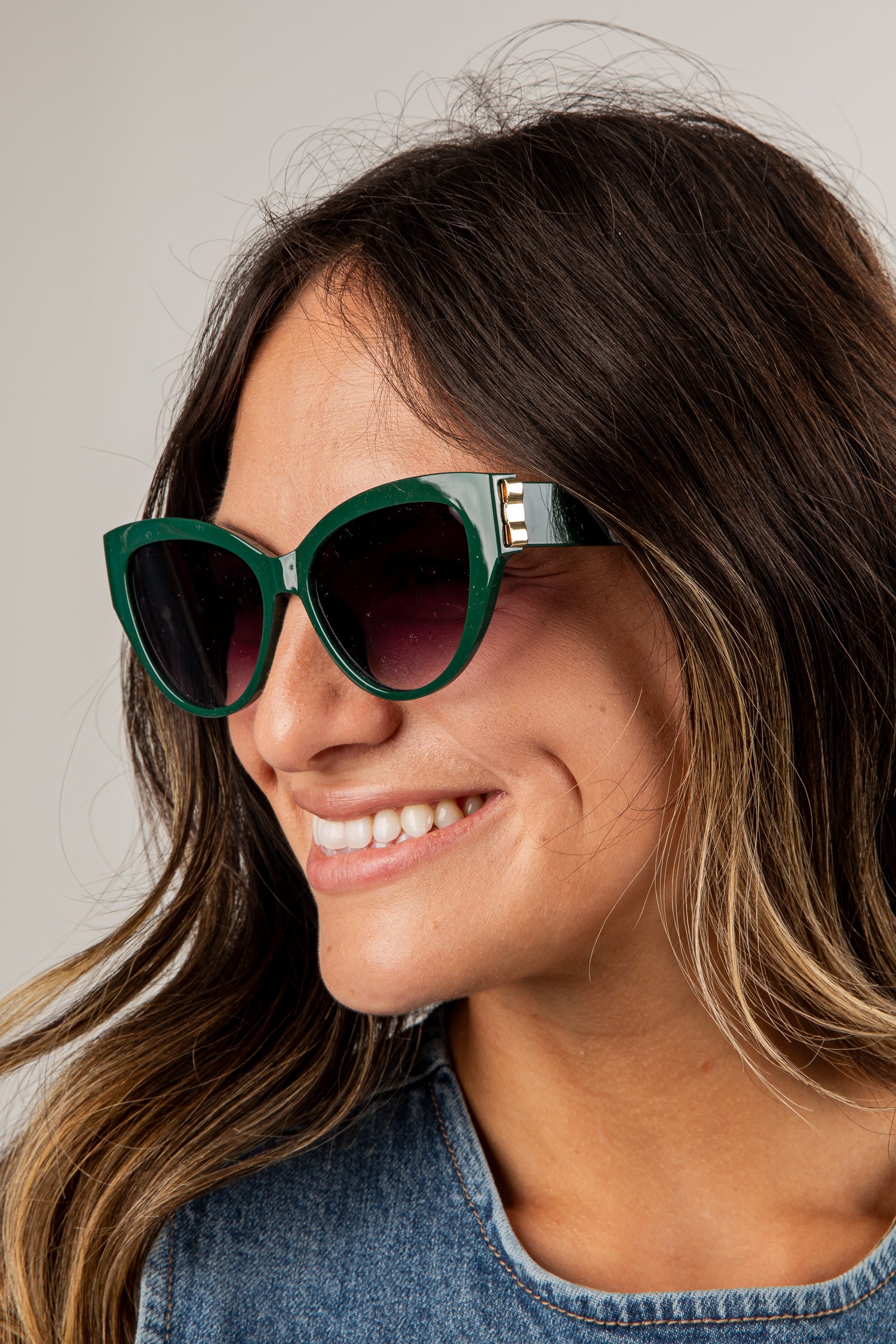 Woman wearing green sunglasses with a neutral background