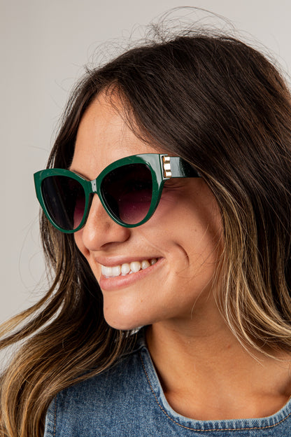 Woman wearing green sunglasses with a neutral background