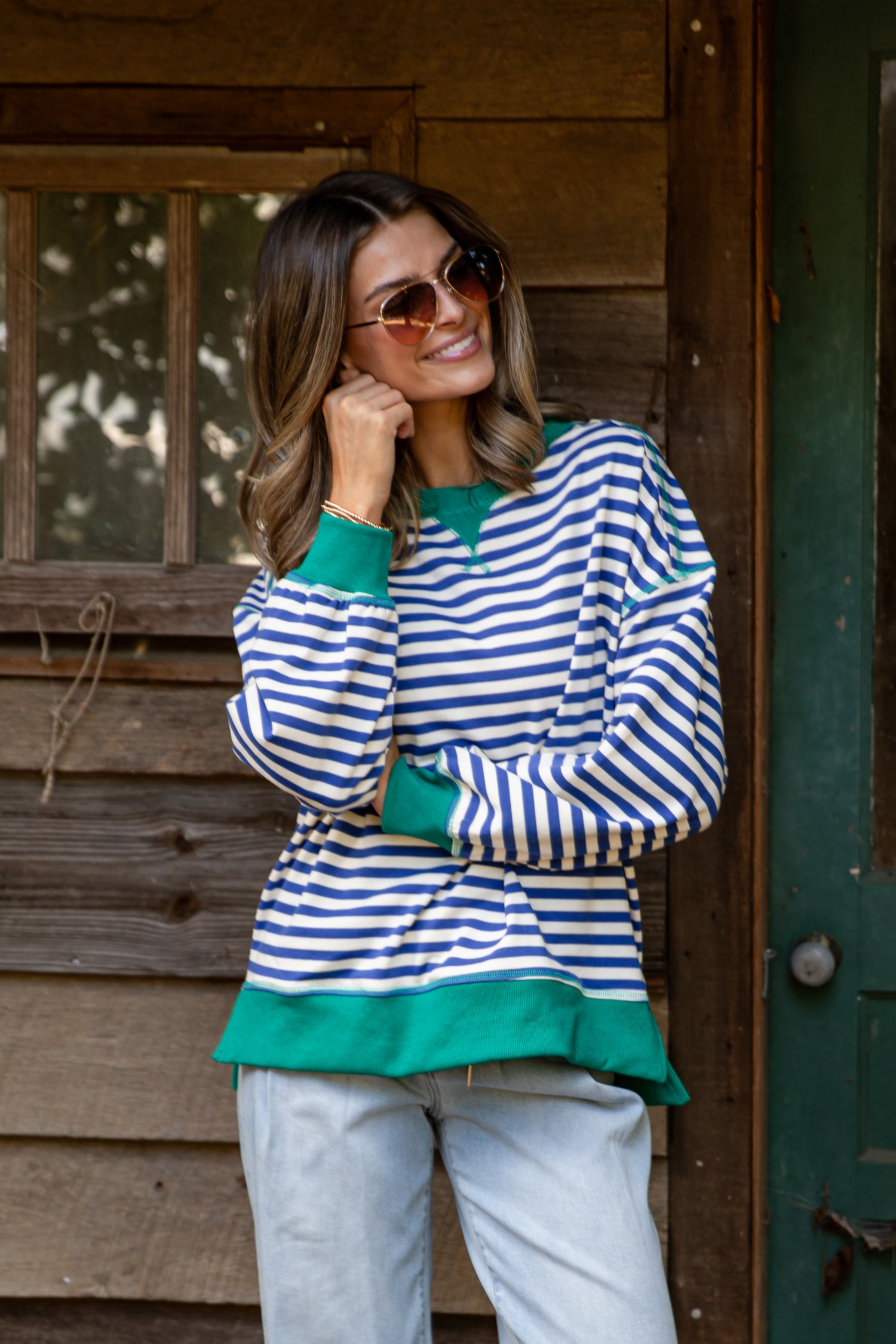 Woman wearing a striped sweater with green accents standing in front of a wooden cabin.
