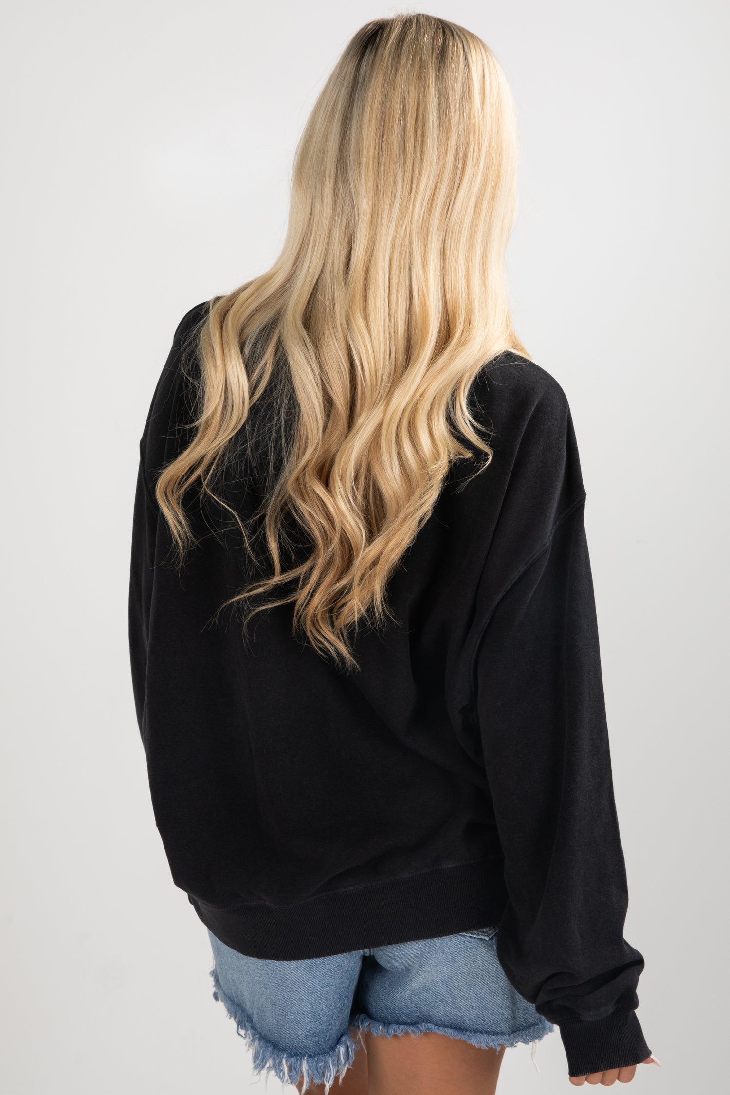 Person wearing a black hoodie and denim shorts on a plain background