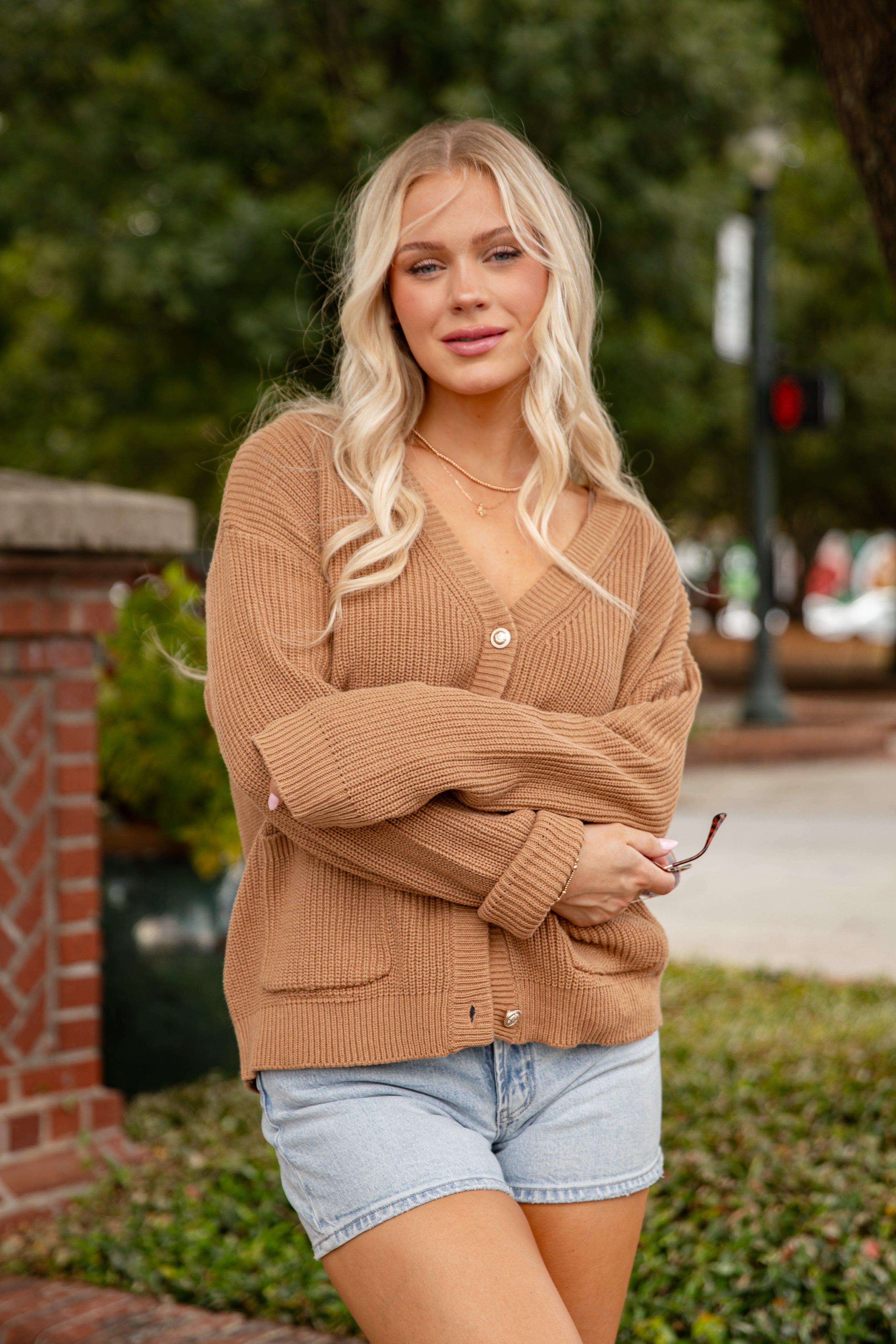 Woman wearing a brown cardigan and denim shorts standing outdoors.