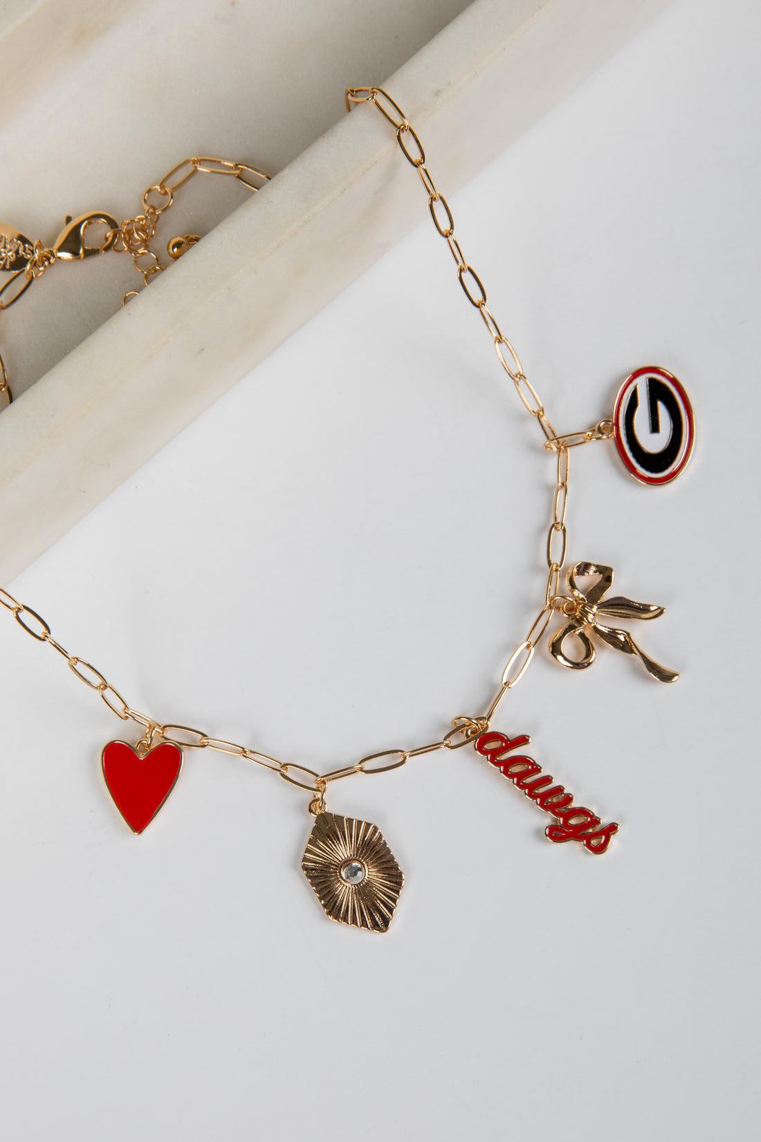 Gold bracelet with various charms including a heart, bow, and word charm on a white surface.