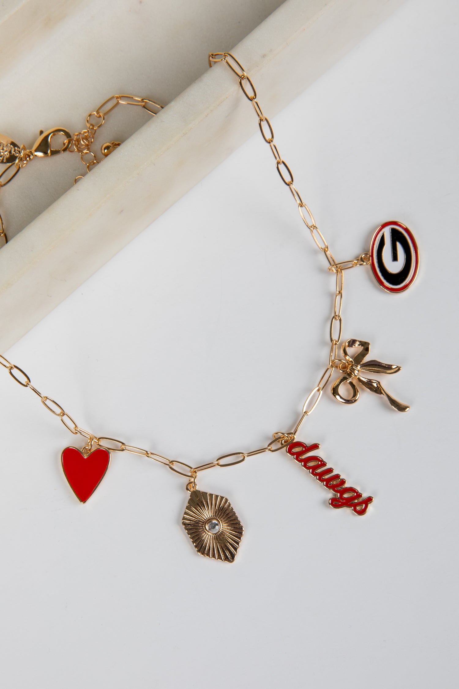 Gold bracelet with various charms including a heart, bow, and word charm on a white surface.