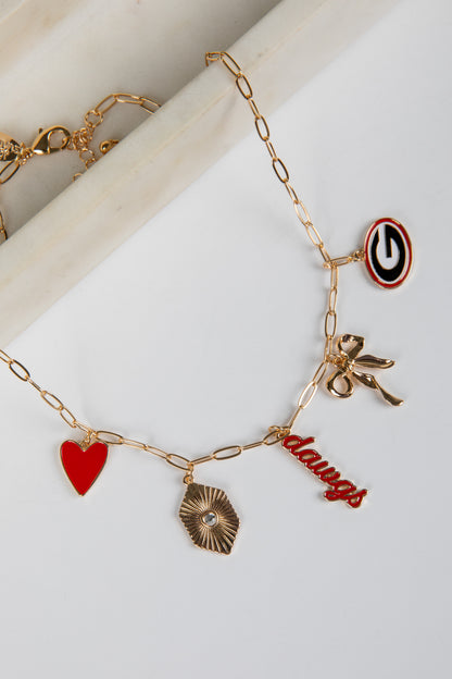 Gold bracelet with various charms including a heart, bow, and word charm on a white surface.