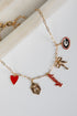 Gold bracelet with various charms including a heart, bow, and word charm on a white surface.