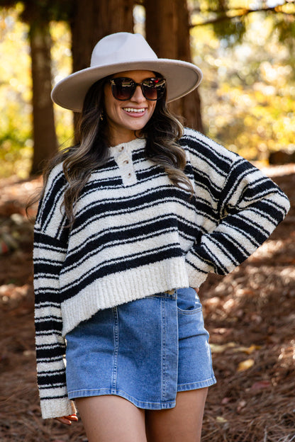 Woman wearing a striped sweater, denim skirt, and hat in a forest setting