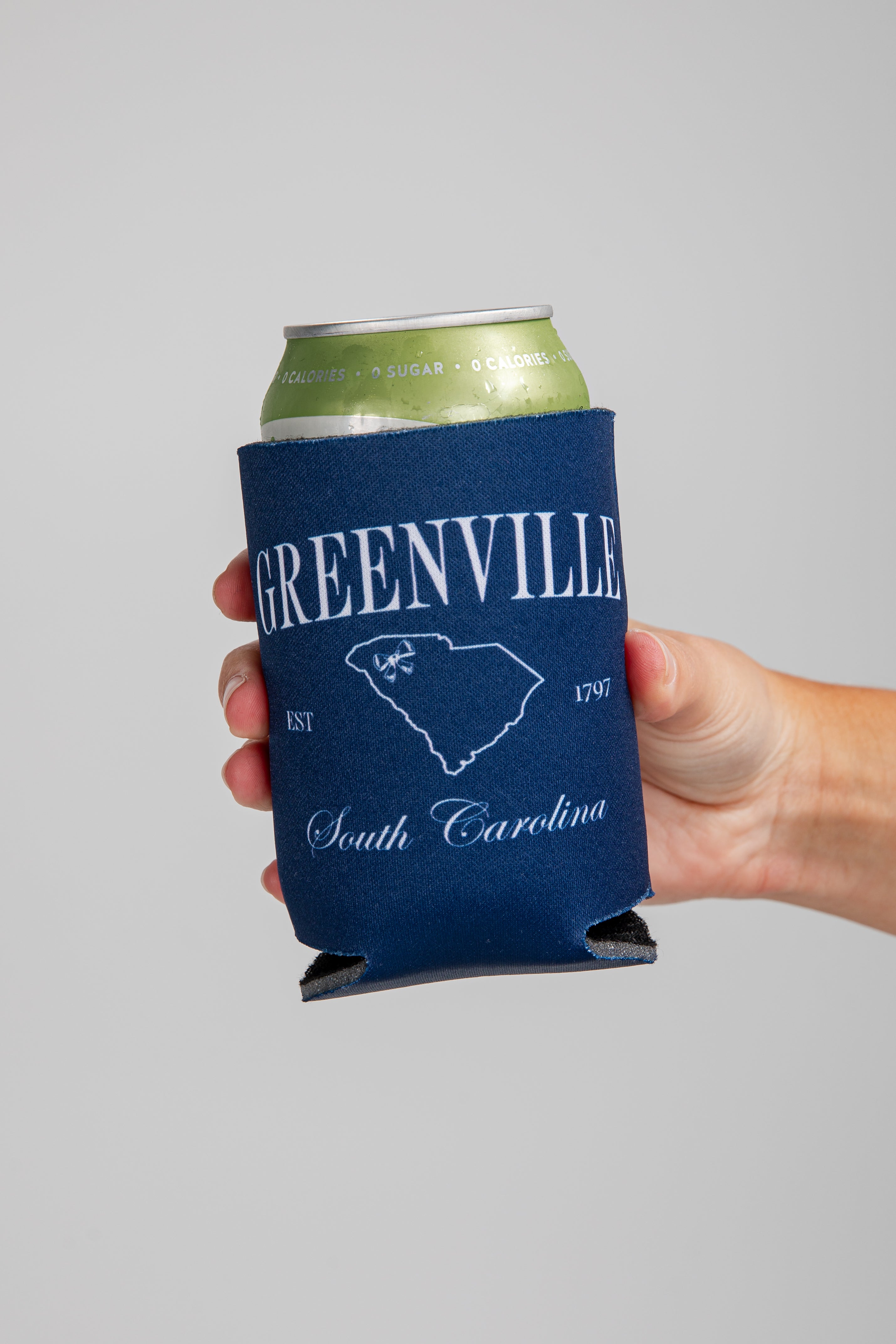 Hand holding a can with a blue Greenville, South Carolina koozie.