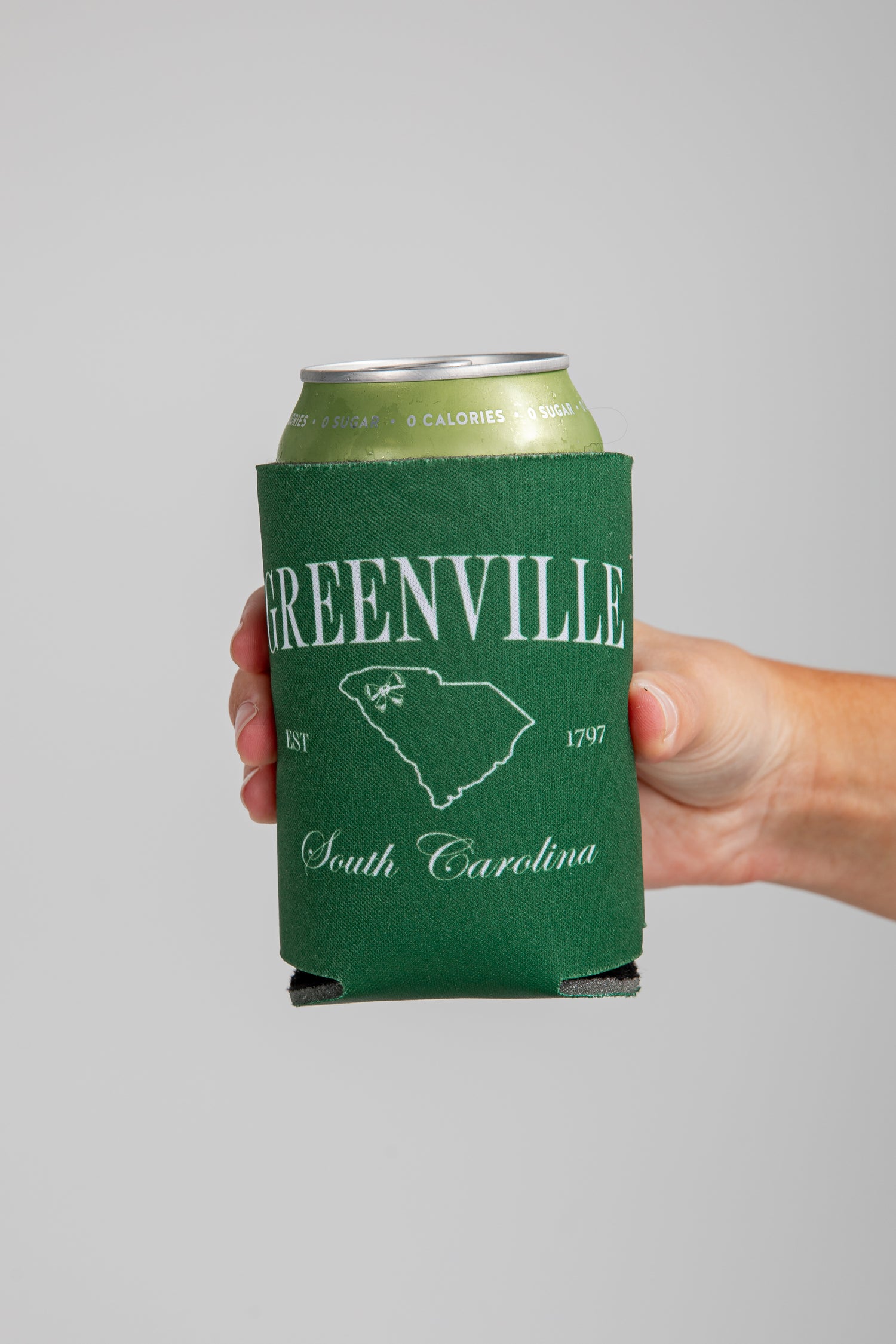 Hand holding a can with a Greenville, South Carolina design on a gray background