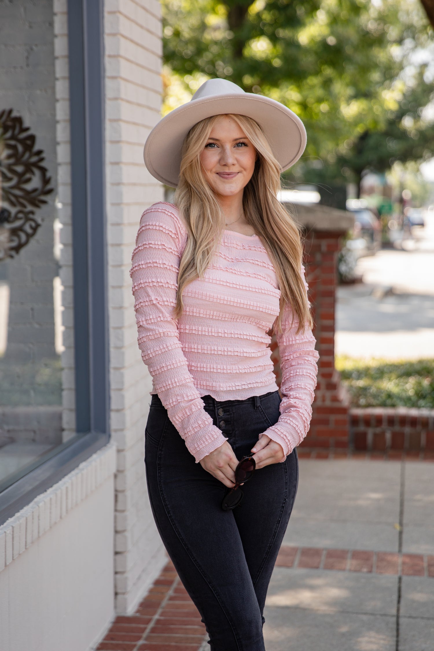Woman wearing a pink sweater and white hat standing on a sidewalk.