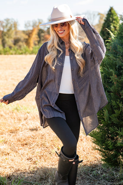 Woman in a gray coat and black boots standing in a field with trees in the background