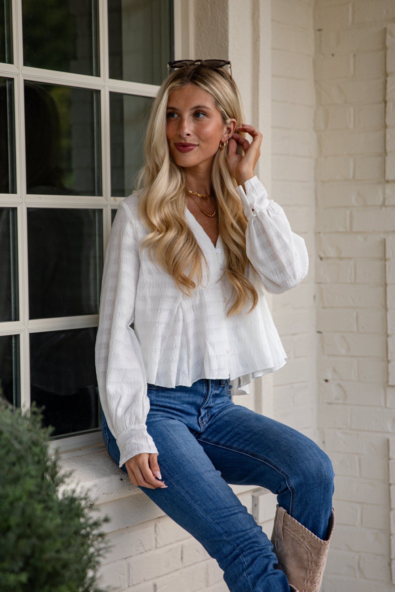 Woman wearing a white blouse and blue jeans sitting on a step.
