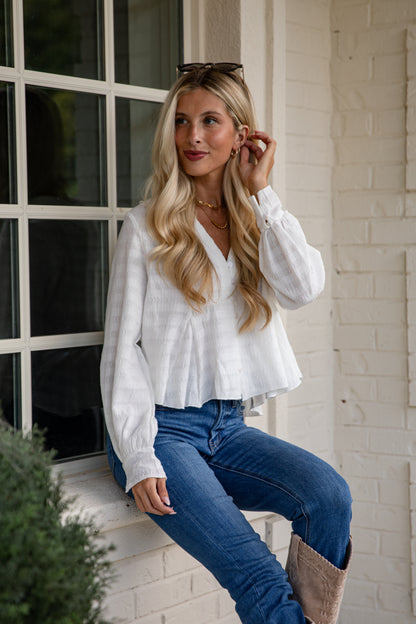 Woman wearing a white blouse and blue jeans sitting on a step.